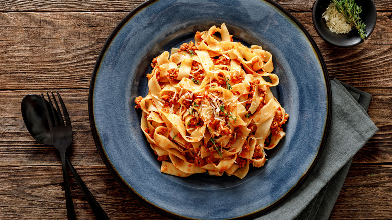 Pasta with sauce atop blue plate on wooden table