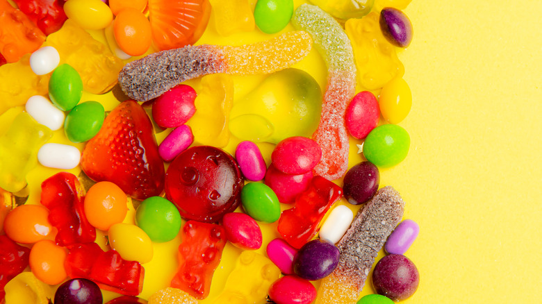 Assorted colorful candies and gummies on yellow background