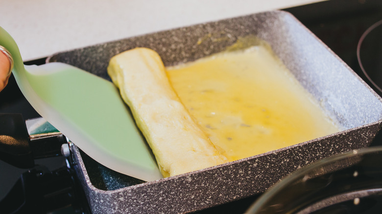 Tamagoyaki being rolled in a tamagoyaki pan