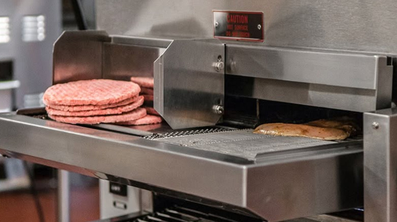Chicken and burger patties going into a Nieco-built flame broiler with a conveyor belt