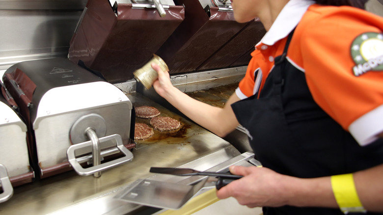 An employee inside a McDonald's seasons burger patties on a clamshell grill