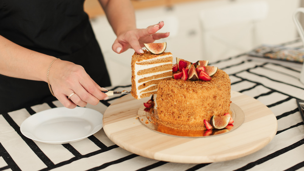 Baker cutting into a layered honey cake
