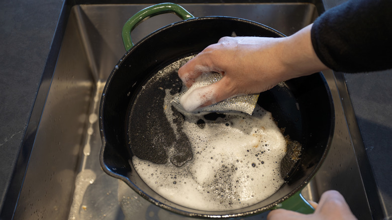 Cleaning cast-iron skillet with soap in sink