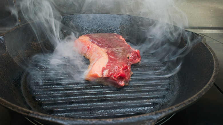 Cast-iron pan smoking with raw steak