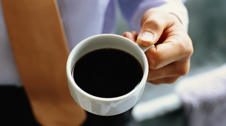 Person holding a small cup of black coffee