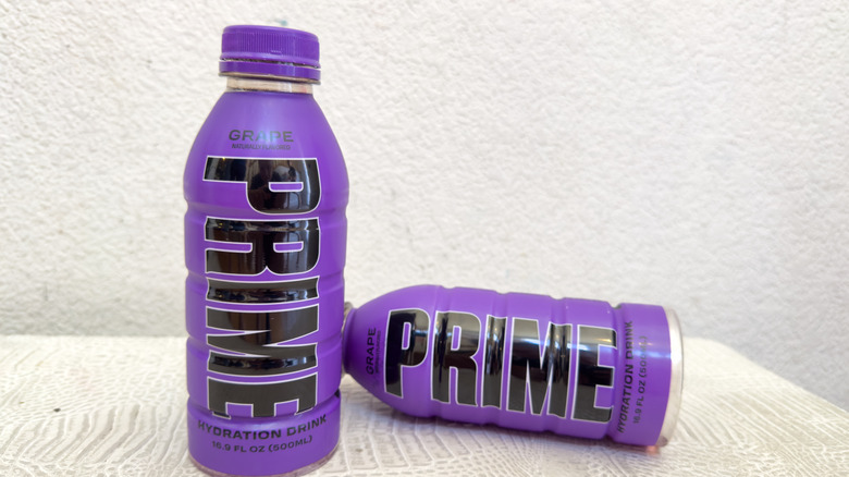 Two bottles of PRIME Grape flavor against a wall