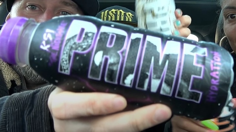 Three people in a car holding up a PRIME bottle in KSI The Nightmare flavor