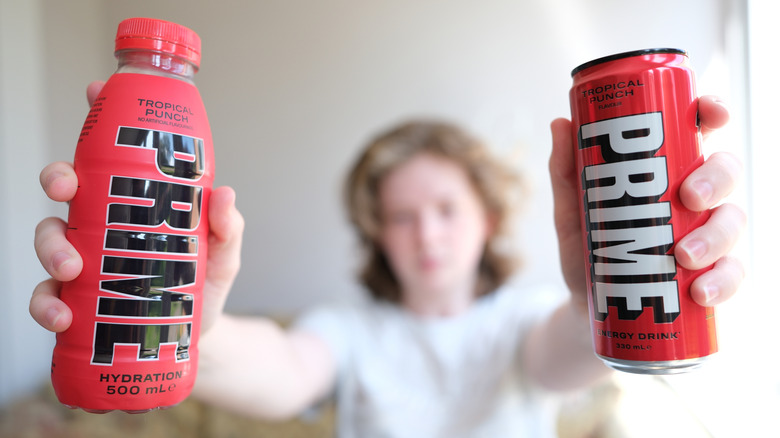 A person holding up a bottle of PRIME Hydration and a can of PRIME Energy