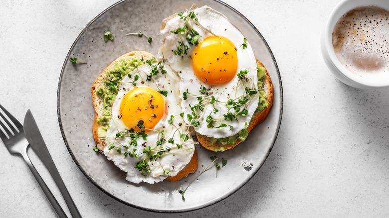 Fried eggs on avocado toast with a cup of coffee