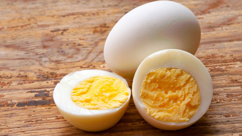 Hard-boiled eggs, one cut in half on wooden table