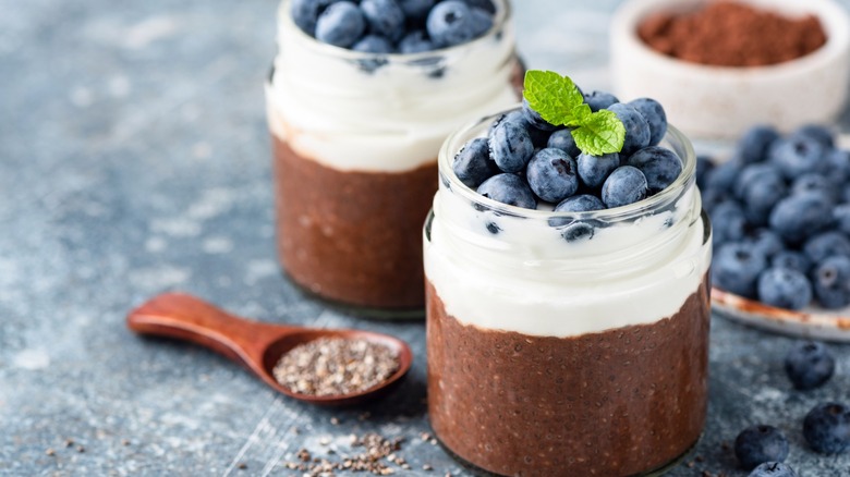 Two jars of chocolate pudding with whipped cream and blueberries on top