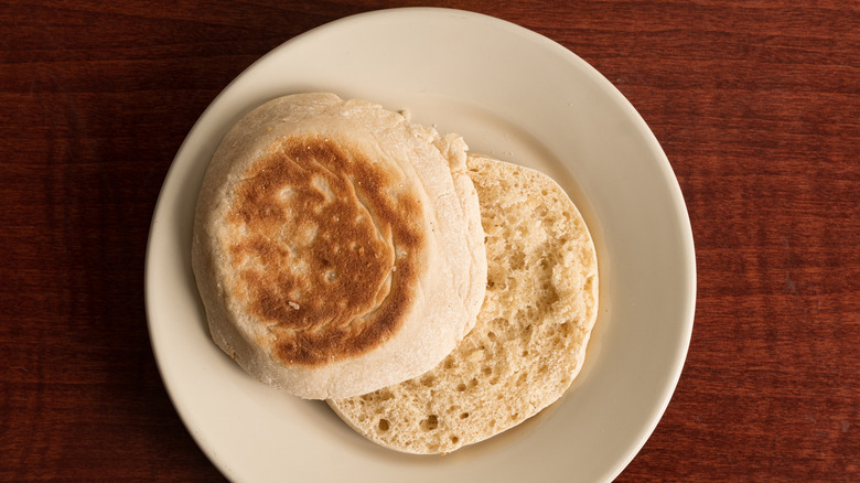 A sliced English muffin on a white plate on a wooden table