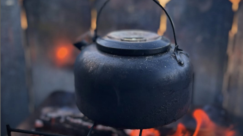 A modern camp kettle over a fire pit.