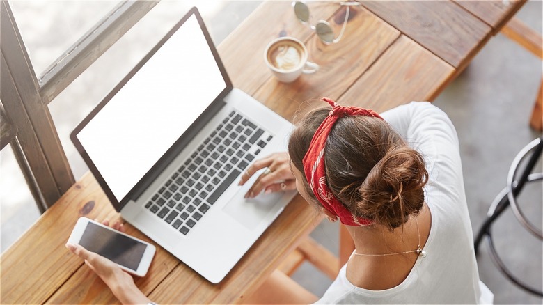 Woman working in coffee shop with coffee, laptop, and phone