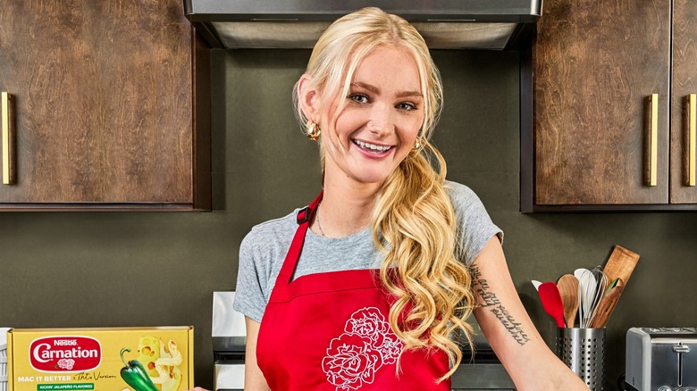 Tineke Younger smiles while posing for a photo in a chef's apron in a kitchen