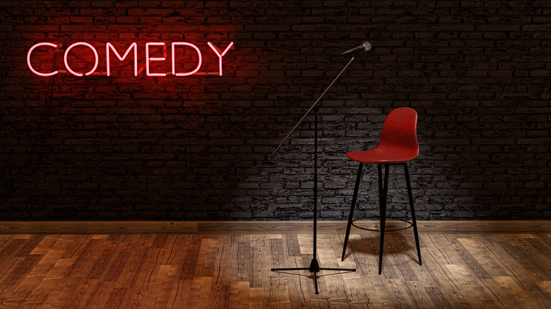 a microphone stand and red chair on a stage with a neon sign in the back that says Comedy