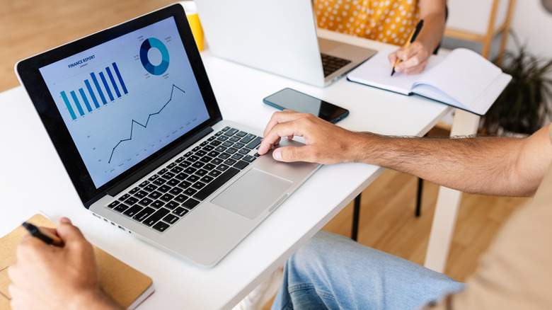 a man sitting with both arms on his a desk and looking at charts and data on his laptop
