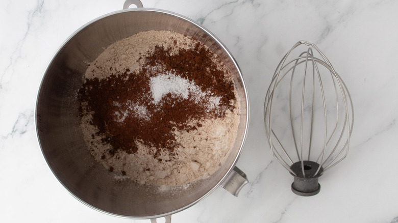 Flours and cocoa powder in mixing bowl next to whisk attachment