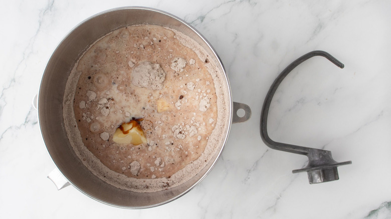Unmixed bread ingredients in bowl next to dough hook attachment