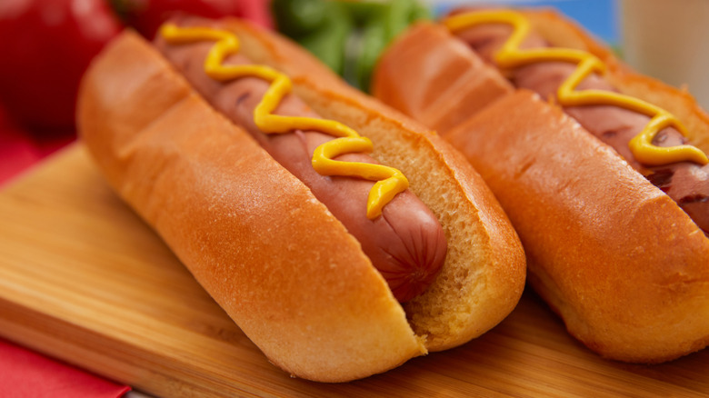 Two hot dogs with mustard on cutting board