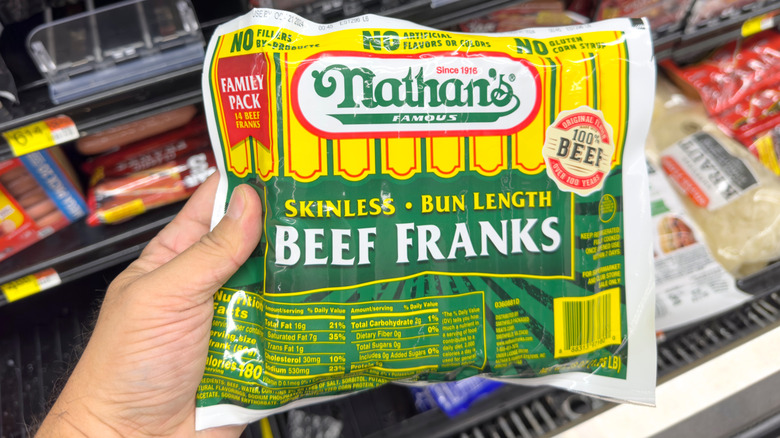 Hand holding package of Nathan's Famous hot dogs in grocery store