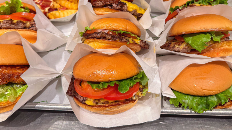 A platter of various burgers with cheese, lettuce, and tomato toppings wrapped in paper