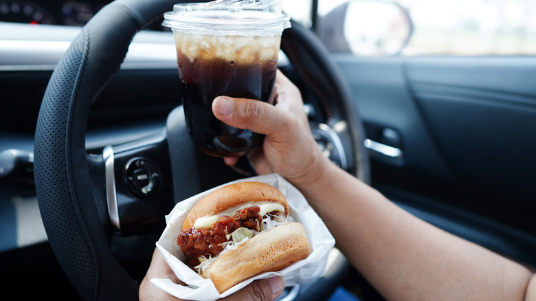 Person holding soda and chicken sandwich in car