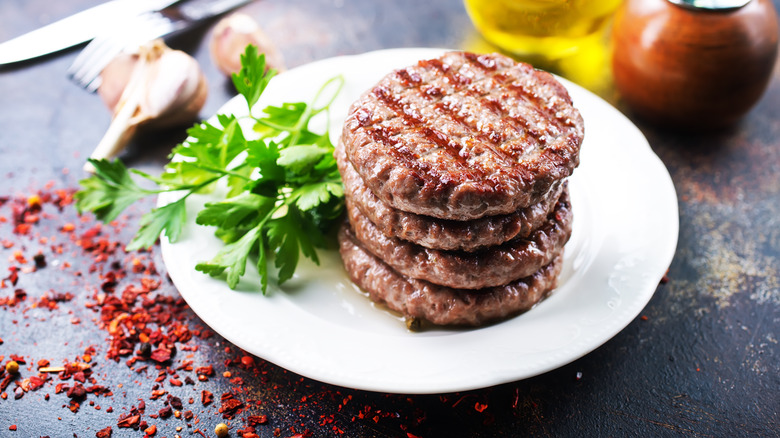   Četiri pljeskavice za hamburger naslagane na bijelom tanjuru sa strane peršina