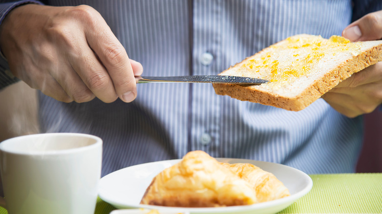 A man's hand spreading marmalade on toast with plate of food