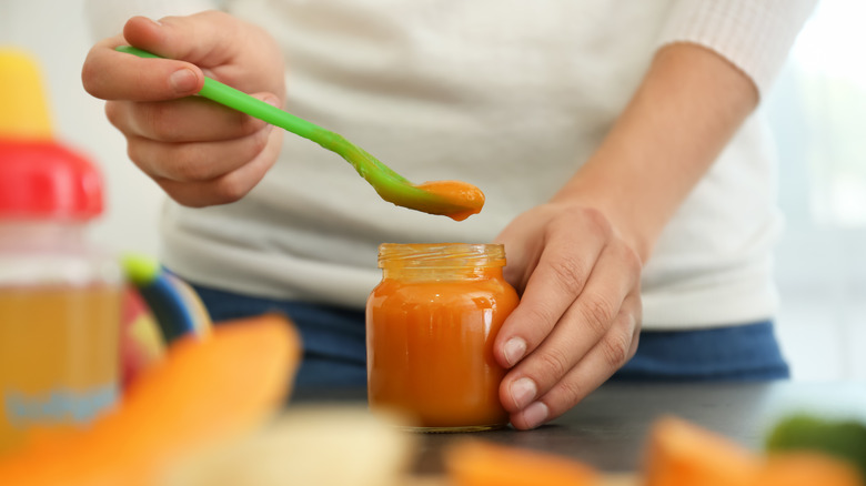 woman spooning baby food from jar