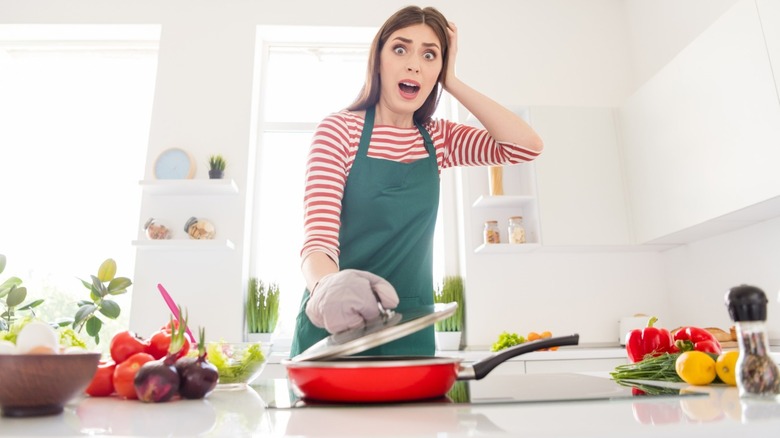 Frightened woman in kitchen holding frying pan lid