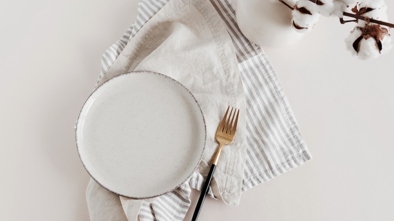 A white plate next to a golden fork over a striped and white napkins