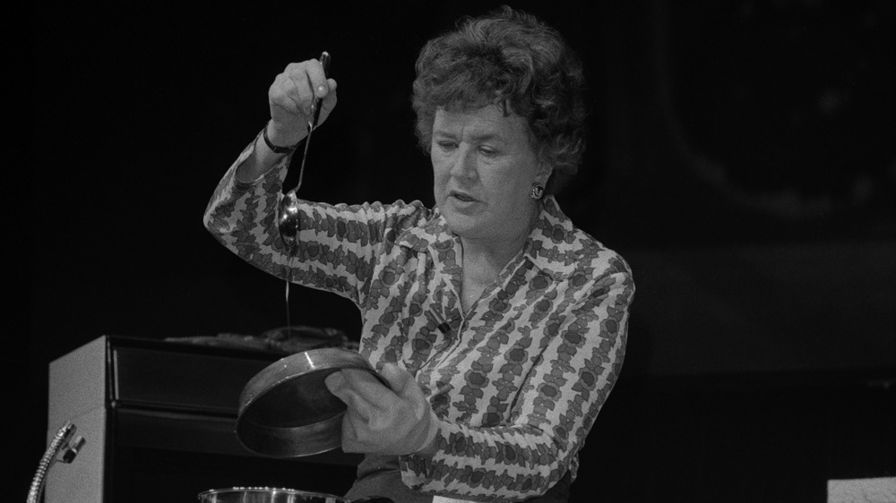 Julia Child holding a spoon and kitchen pan against a black background