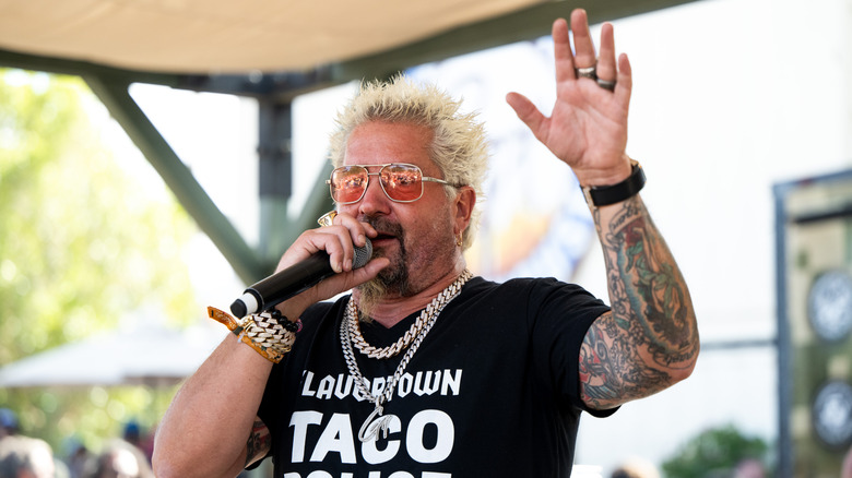 guy fieri speaking into microphone, hand raised