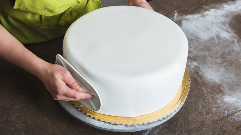 Baker smoothing fondant over cake