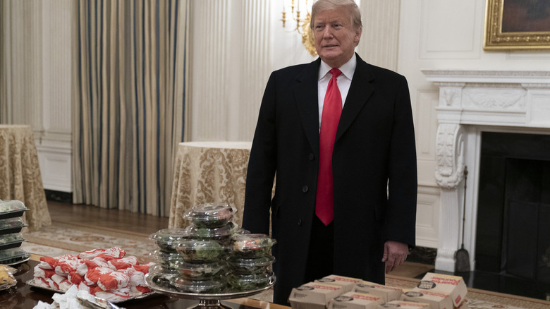 Trump standing before a pile of fast food hamburgers.