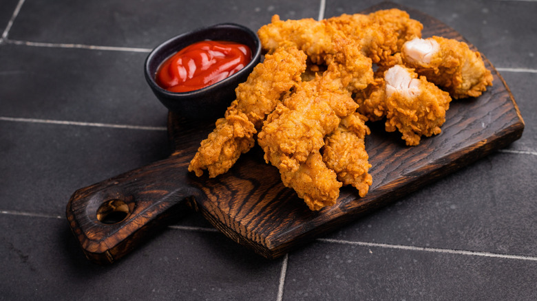Fried chicken tenders on wooden cutting board with sauce