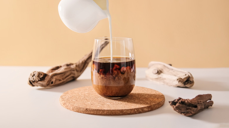 Pitcher of milk pouring into clear cup of coffee