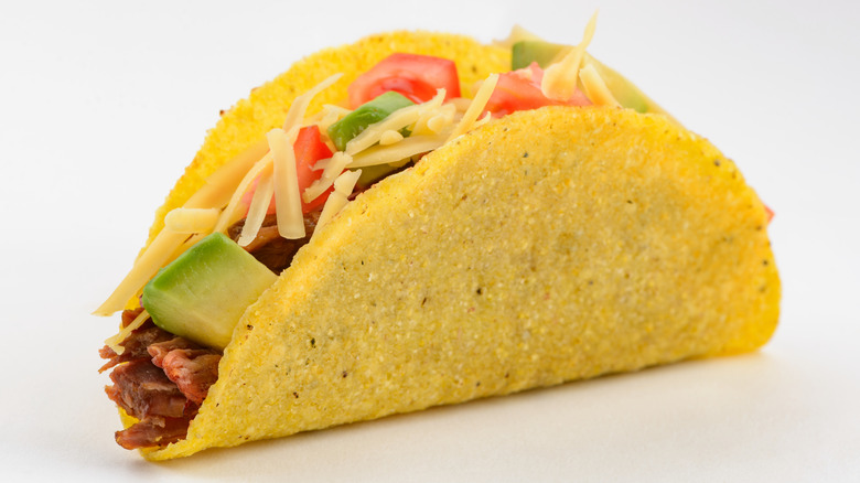 Hard-shell taco filled with beef, avocado, tomatoes, and cheese