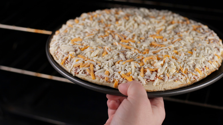 Person putting frozen pizza into oven