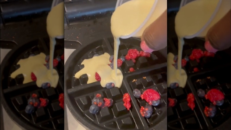 Person adding batter to waffle maker filled with berries