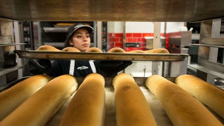 Jimmy John's employee putting tray of French bread on a rack