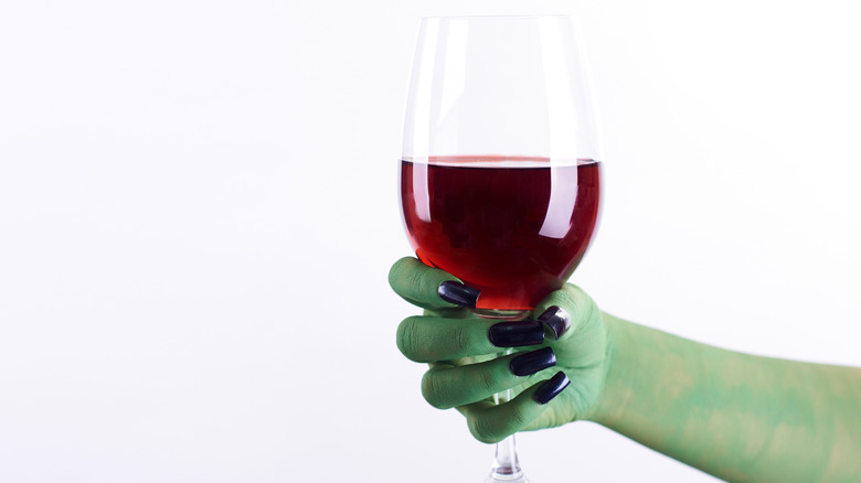 A green hand holding a bottle of red wine