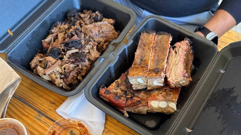 Two black takeout containers filled with pulled beef brisket and pork ribs on a wooden table