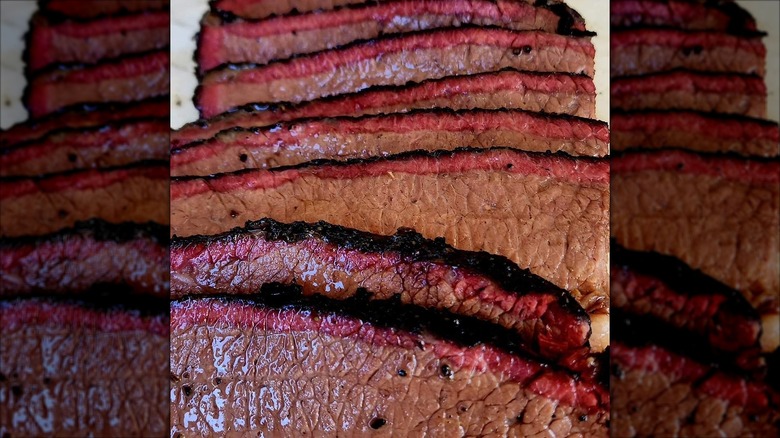 A close-up of thinly sliced, smoked beef brisket with a dark, seasoned bark and a bright pink smoke ring