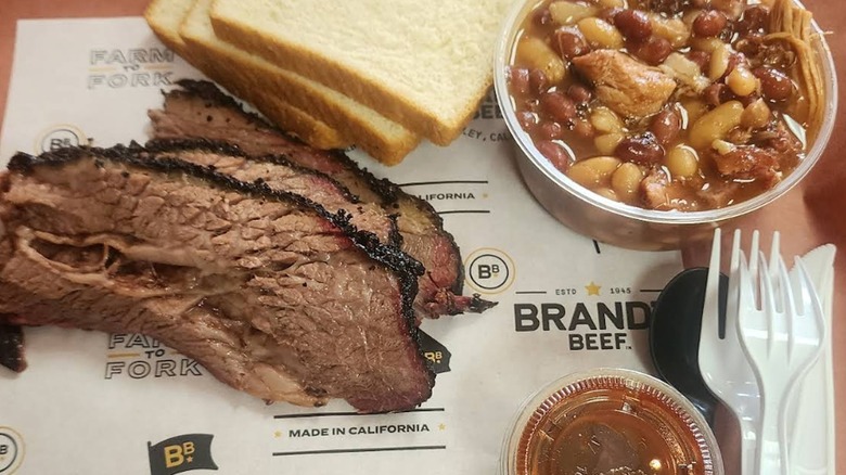 An overhead shot of sliced brisket with a dark bark, served on Brandt Beef paper with white bread, baked beans, and barbecue sauce