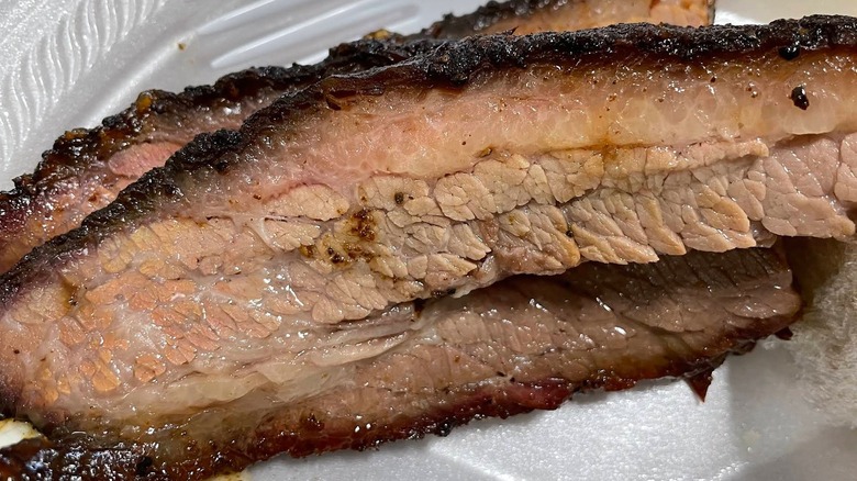 A close-up shot of two thick slices of beef brisket in a white foam container