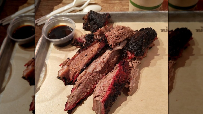A plate of sliced brisket with a bright pink smoke ring and dark bark with a dark sauce on the side