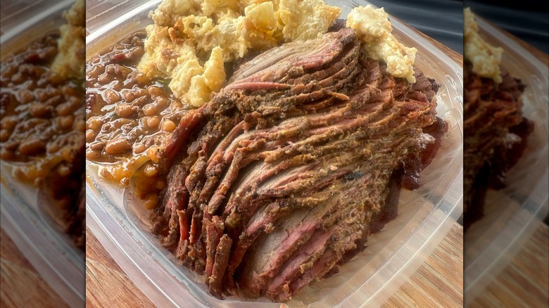 A takeout container of thinly sliced brisket, baked beans, and potato salad