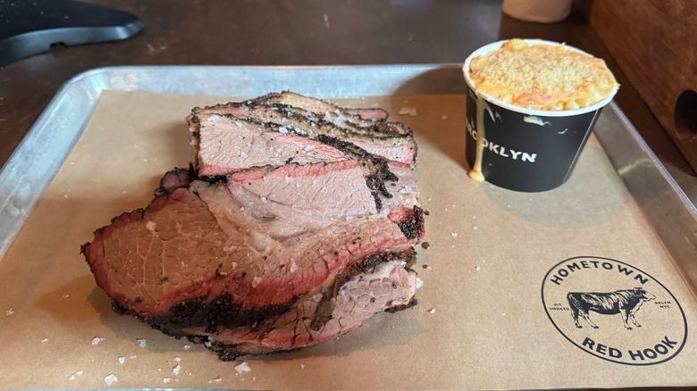 Thick slices of smoked brisket with a dark bark and pink smoke ring on a butcher paper-lined tray, served with a side of mac and cheese